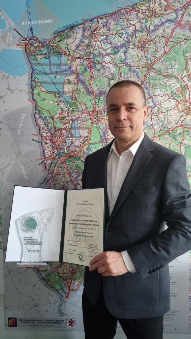 Dyrektor RBGP Województwa Zachodniopomorskiego Leszek Jastrzębski na tle mapy, z dyplomem i statuetką Zielony Feniks 