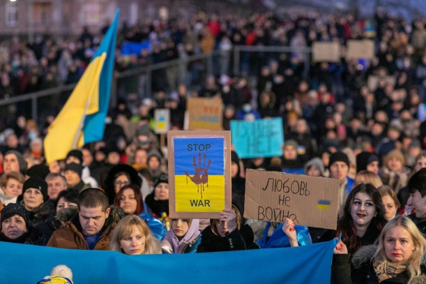 Manifestanci z flagą Ukrainy i transparentami, w tle Filharmonia Szczecińska podświetlona w barwach ukraińskich.
